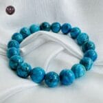 Turquoise crystal bracelet with polished round beads displayed on white satin fabric